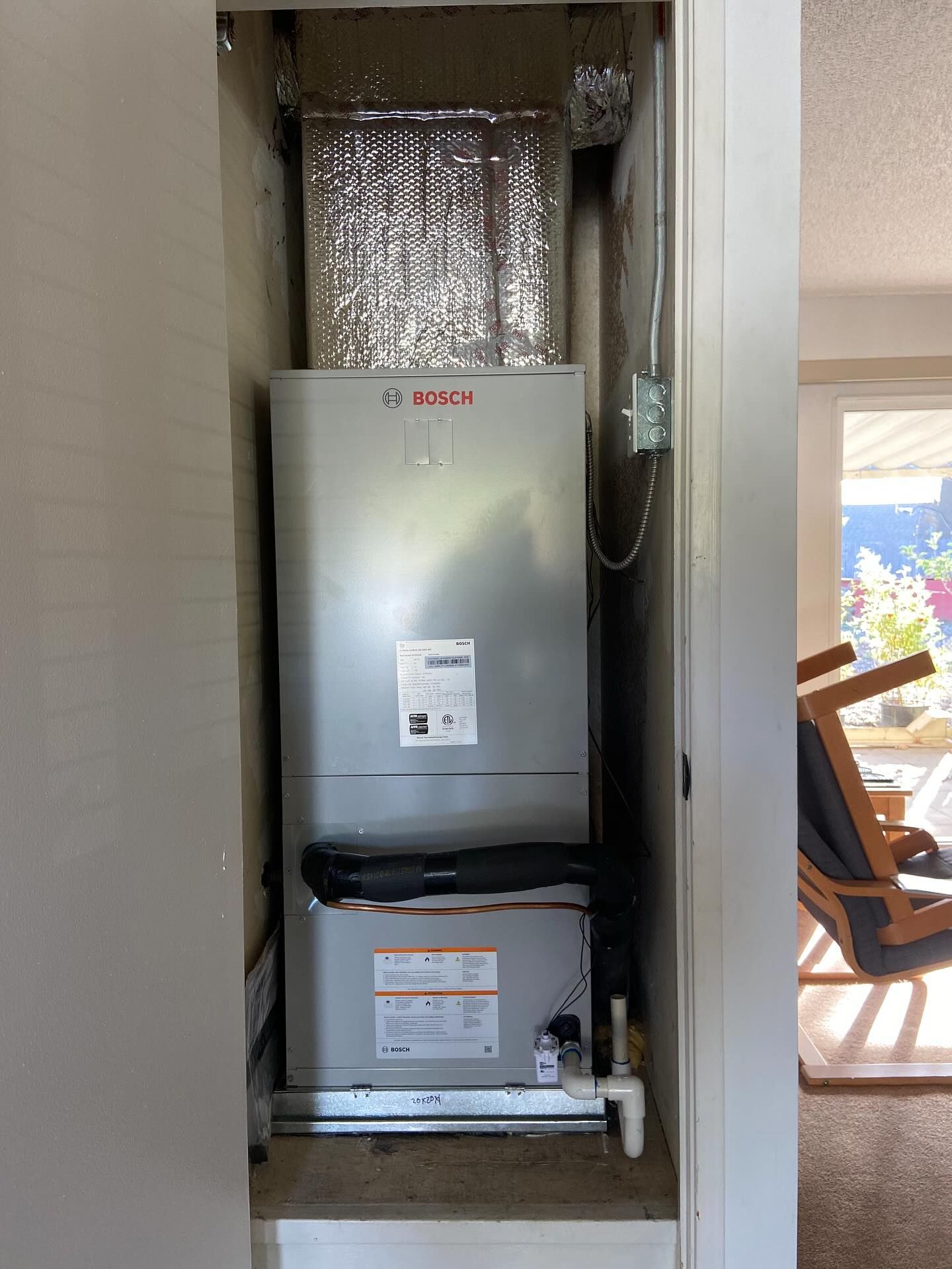 Wall-mounted HVAC unit in a narrow utility closet with exposed ductwork and piping
