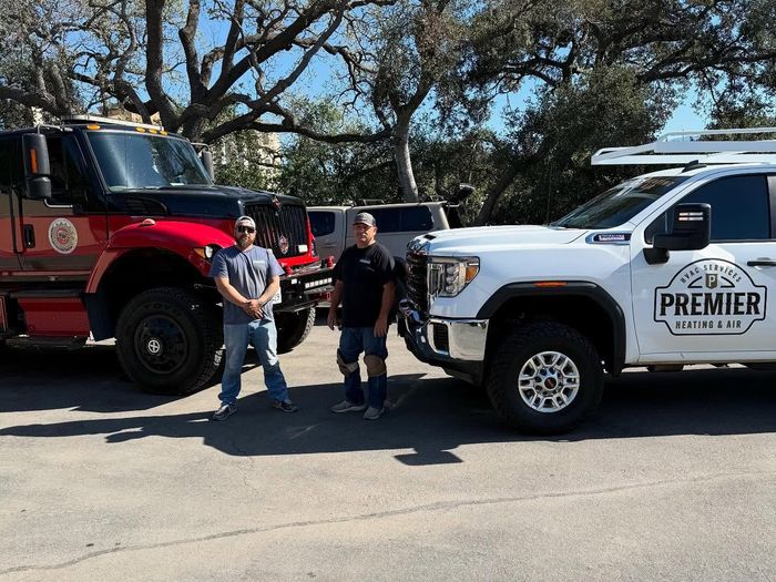 Two workers standing between a red fire truck and a white Premier utility truck on a sunny street
