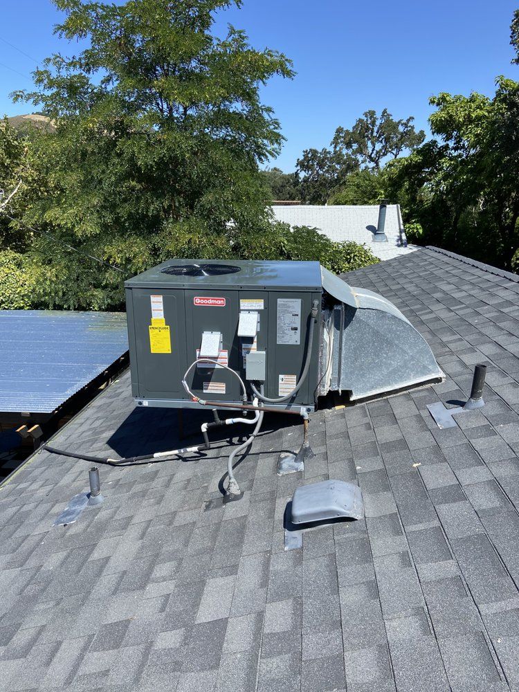 HVAC unit on a shingled roof with ducting and tools, trees in the background