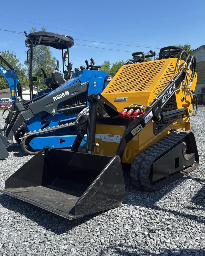 Blue and yellow mini skid steer loaders with bucket attachments on gravel lot