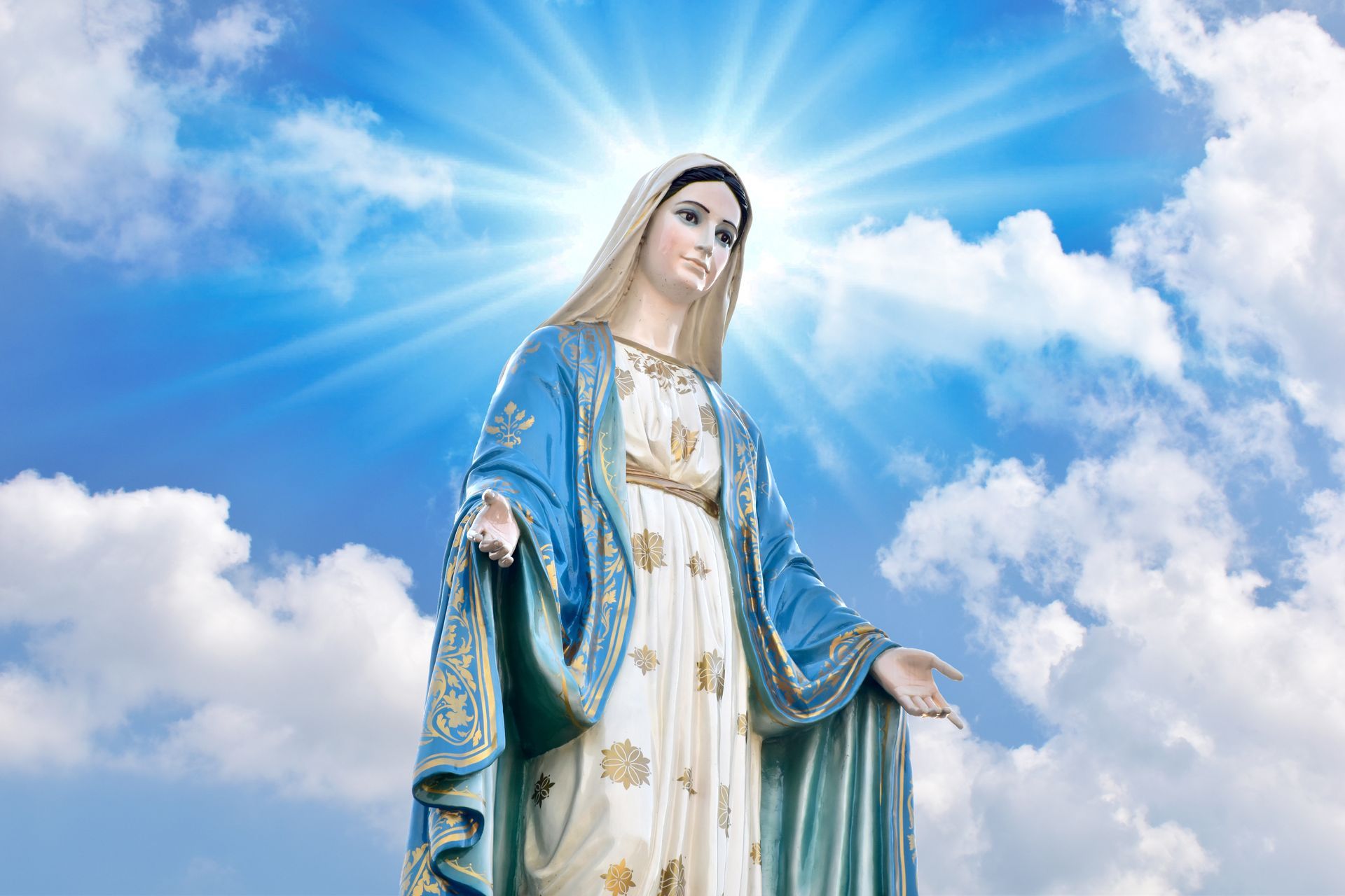 a statue of the virgin mary stands in front of a cloudy sky