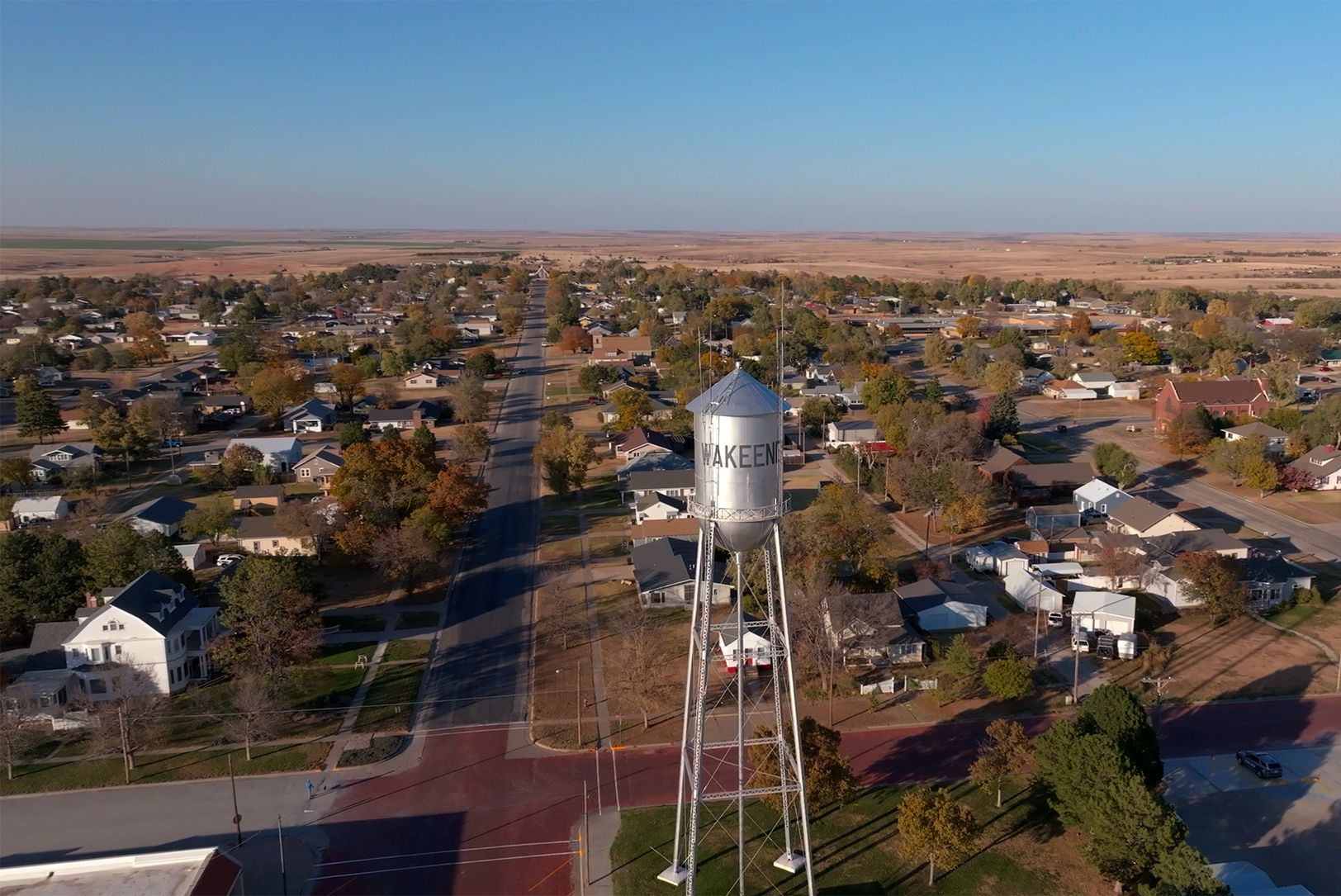 Water tower in a small town. Houses and flat, brown land surround it under a blue sky.