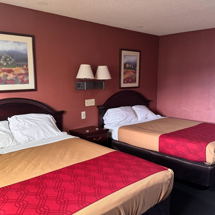 A motel room with two beds, red walls, and landscape paintings.