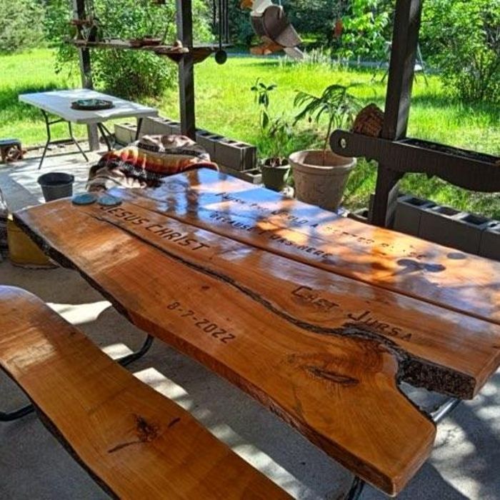 Large wooden picnic table with inscriptions, outdoors.