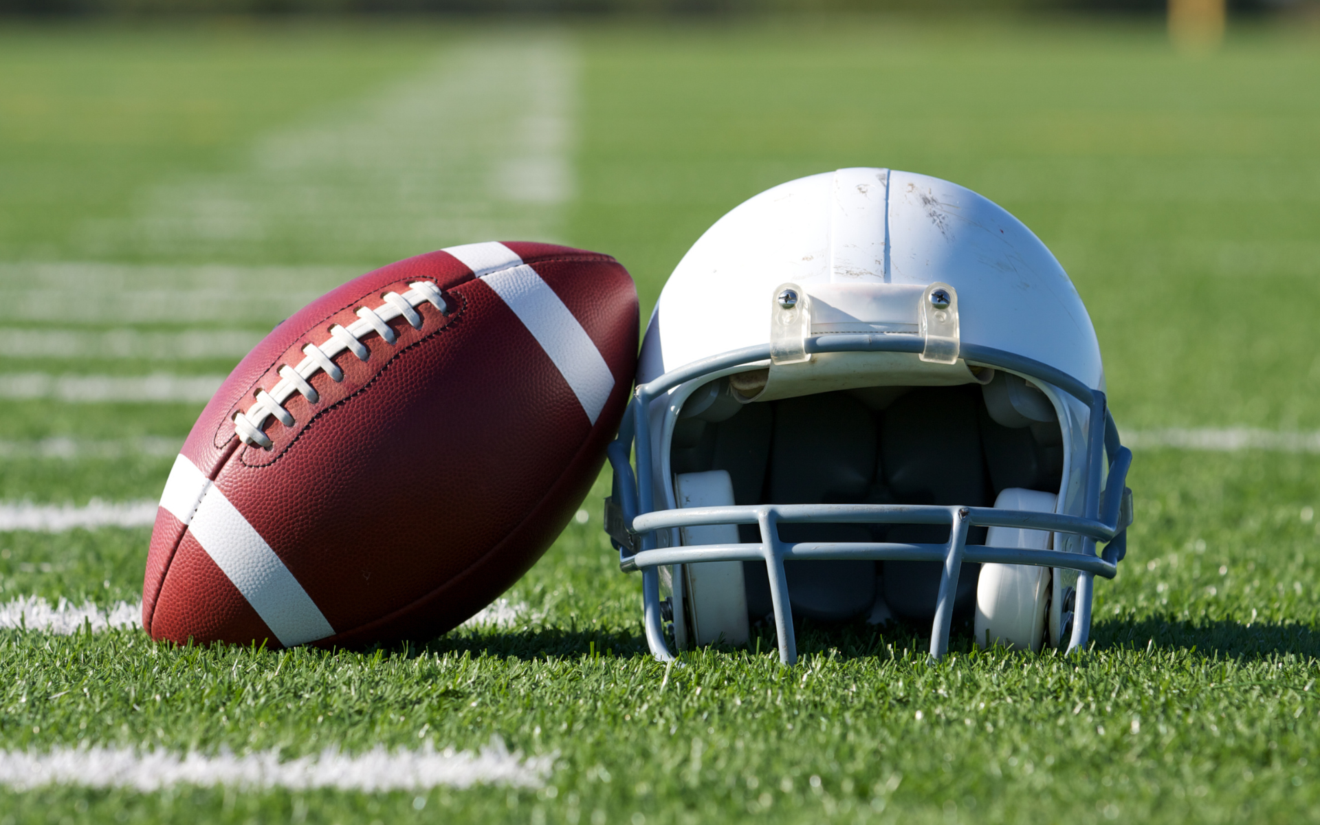 Man with crossed arms on a football field. He is wearing a blue polo shirt, khaki pants, and has a serious expression.