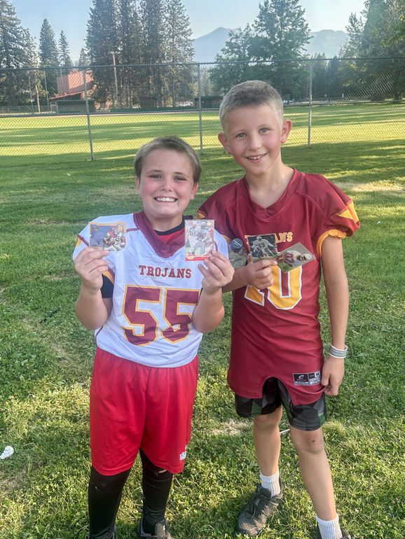 Football players in action on a grassy field; one runs with the ball, pursued by two opponents.