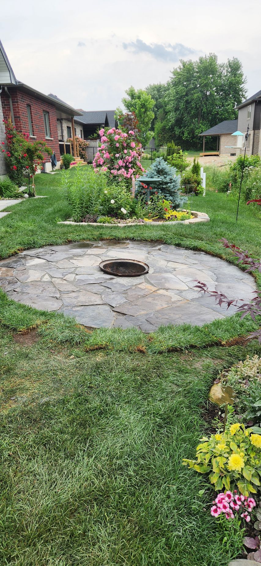 A fire pit in the middle of a lush green yard surrounded by flowers.