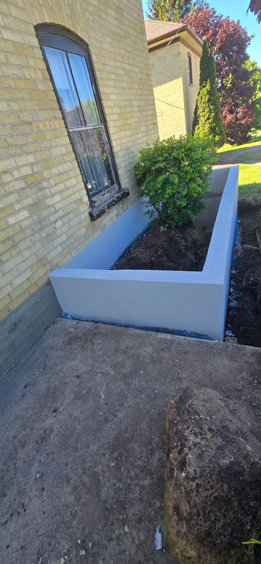 A planter is sitting on the side of a brick building next to a window.