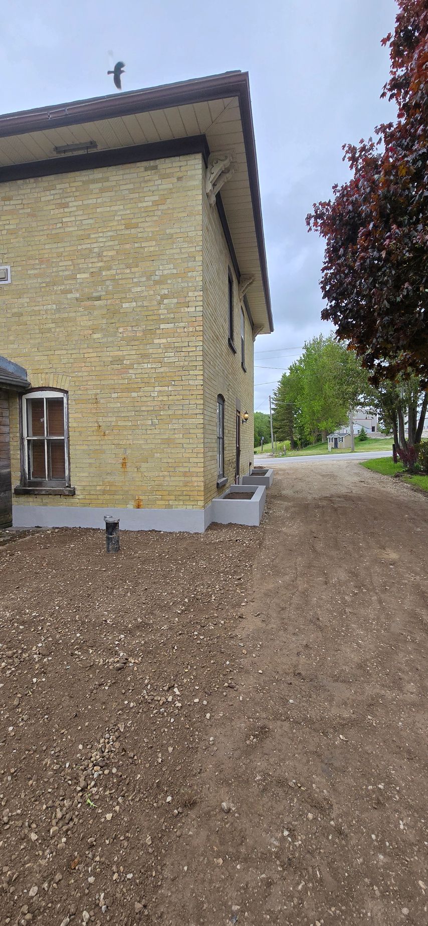 A yellow brick house with a gravel driveway in front of it.