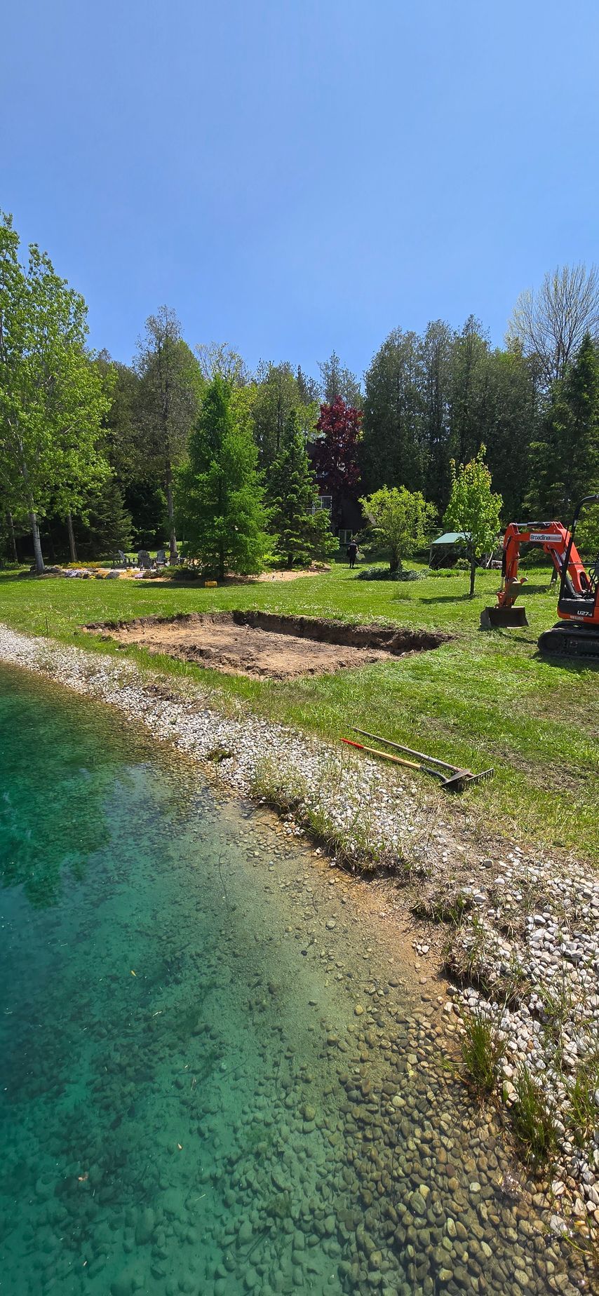 An excavator is sitting on the shore of a lake.
