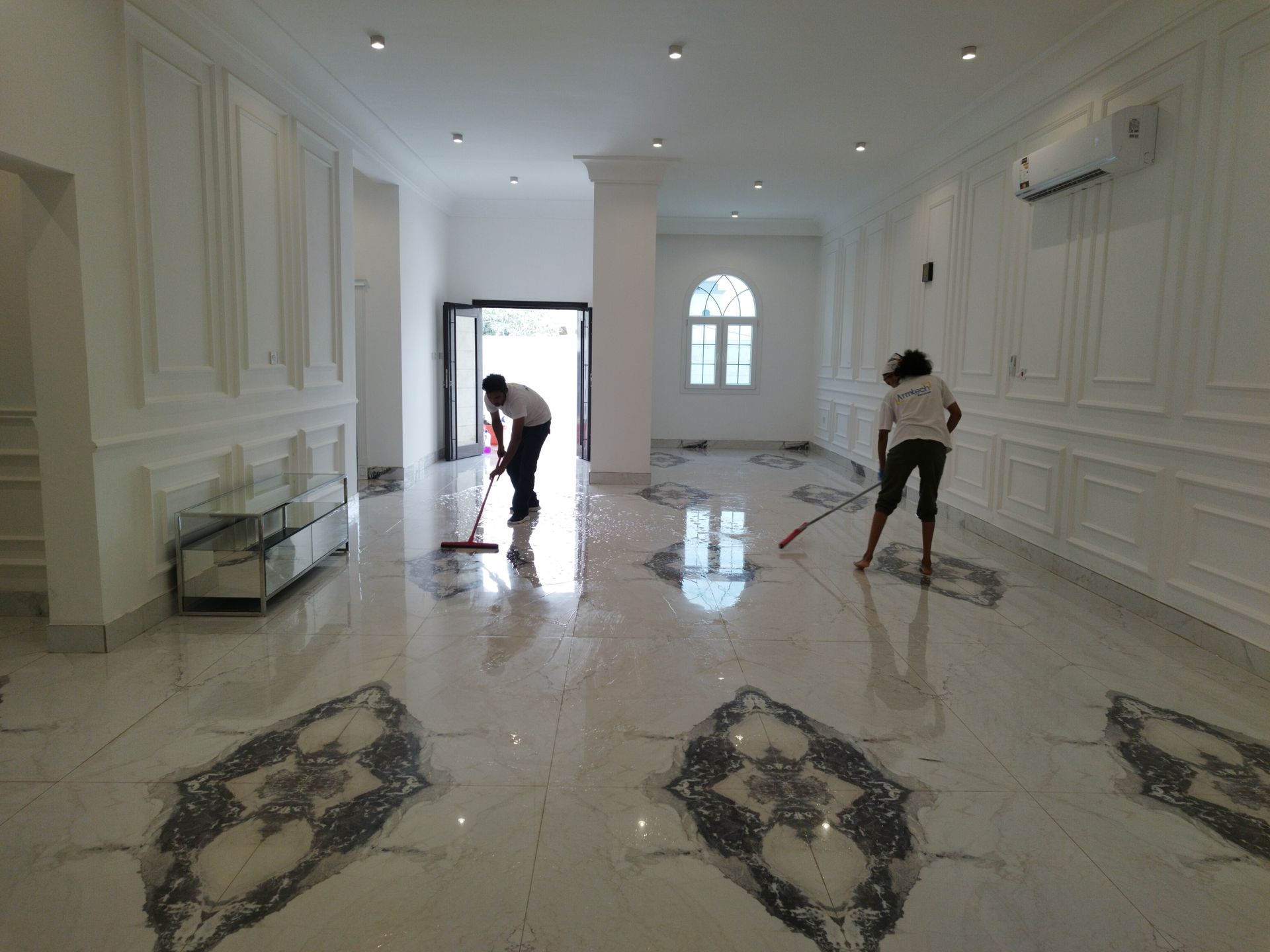 A man and a woman are cleaning a marble floor in a large room.