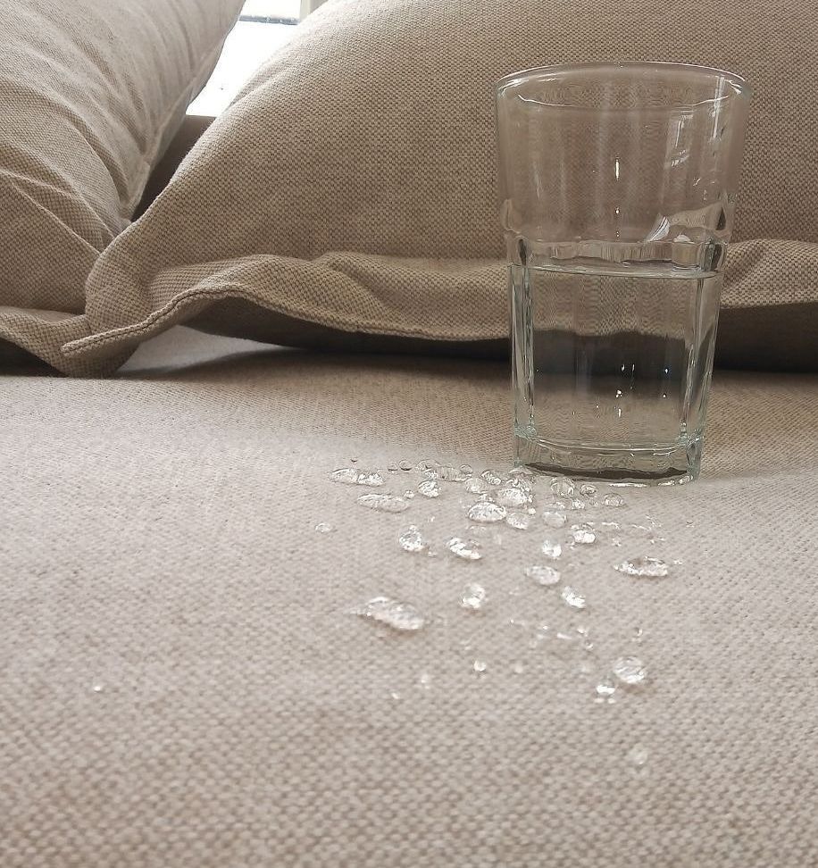 A man in a protective suit is cleaning a couch.