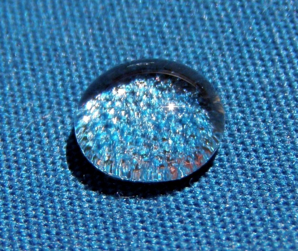 Water droplet on blue fabric, reflecting the fabric's texture and sunlight.