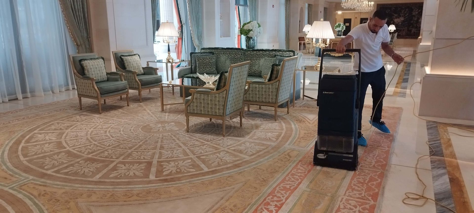 A man in a white shirt is pushing a cart in a room with chairs and a rug.