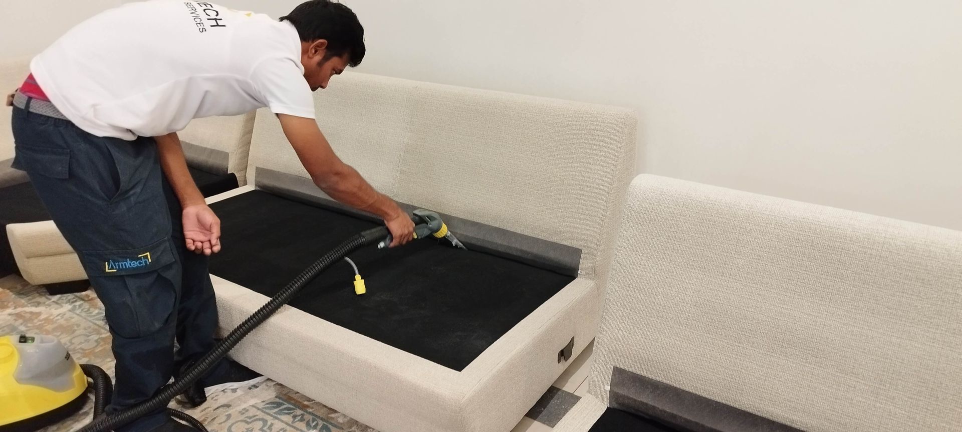 A man is cleaning a couch with a vacuum cleaner.