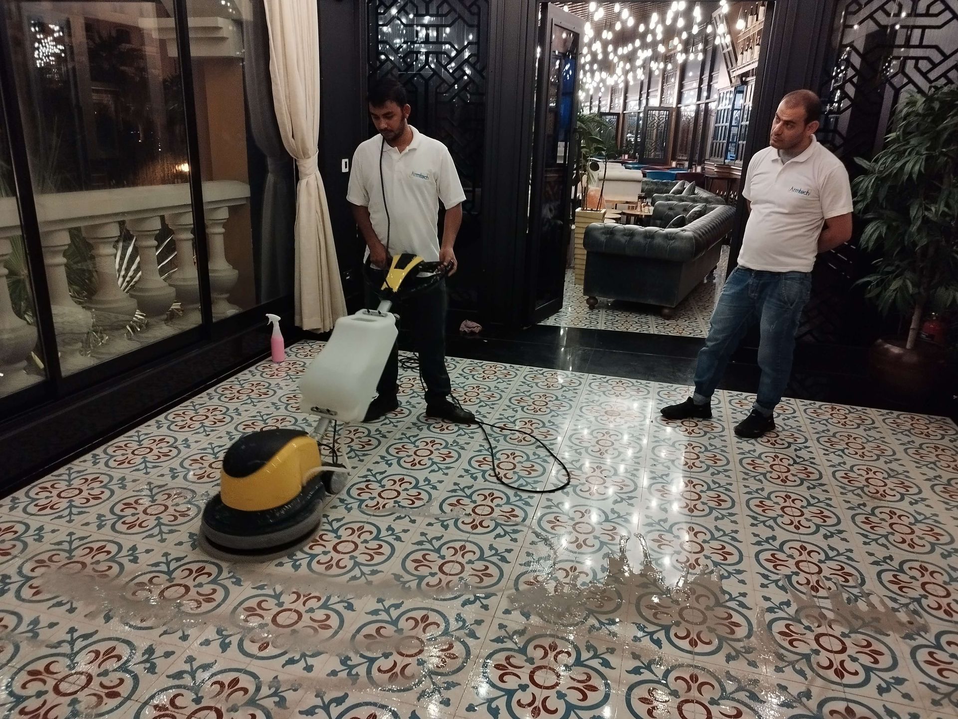 Two men are cleaning a tiled floor with a machine.
