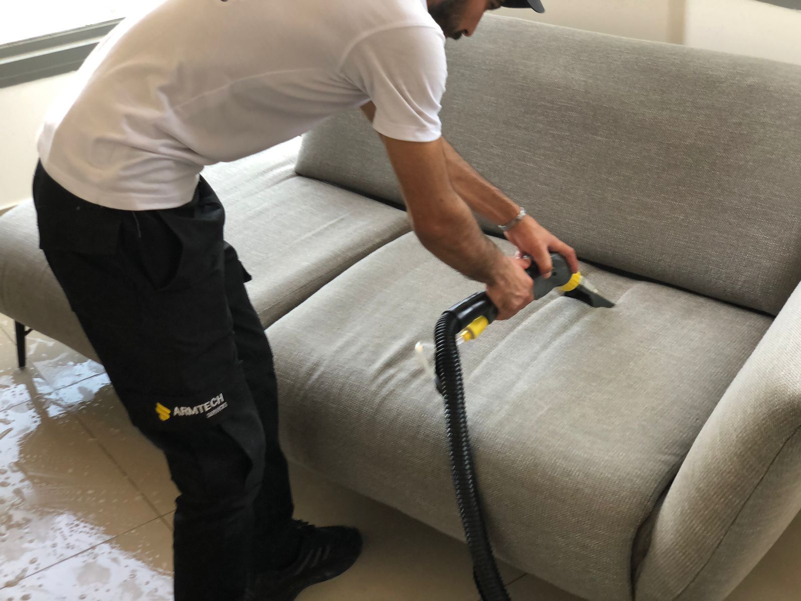 A man is cleaning a couch with a vacuum cleaner.