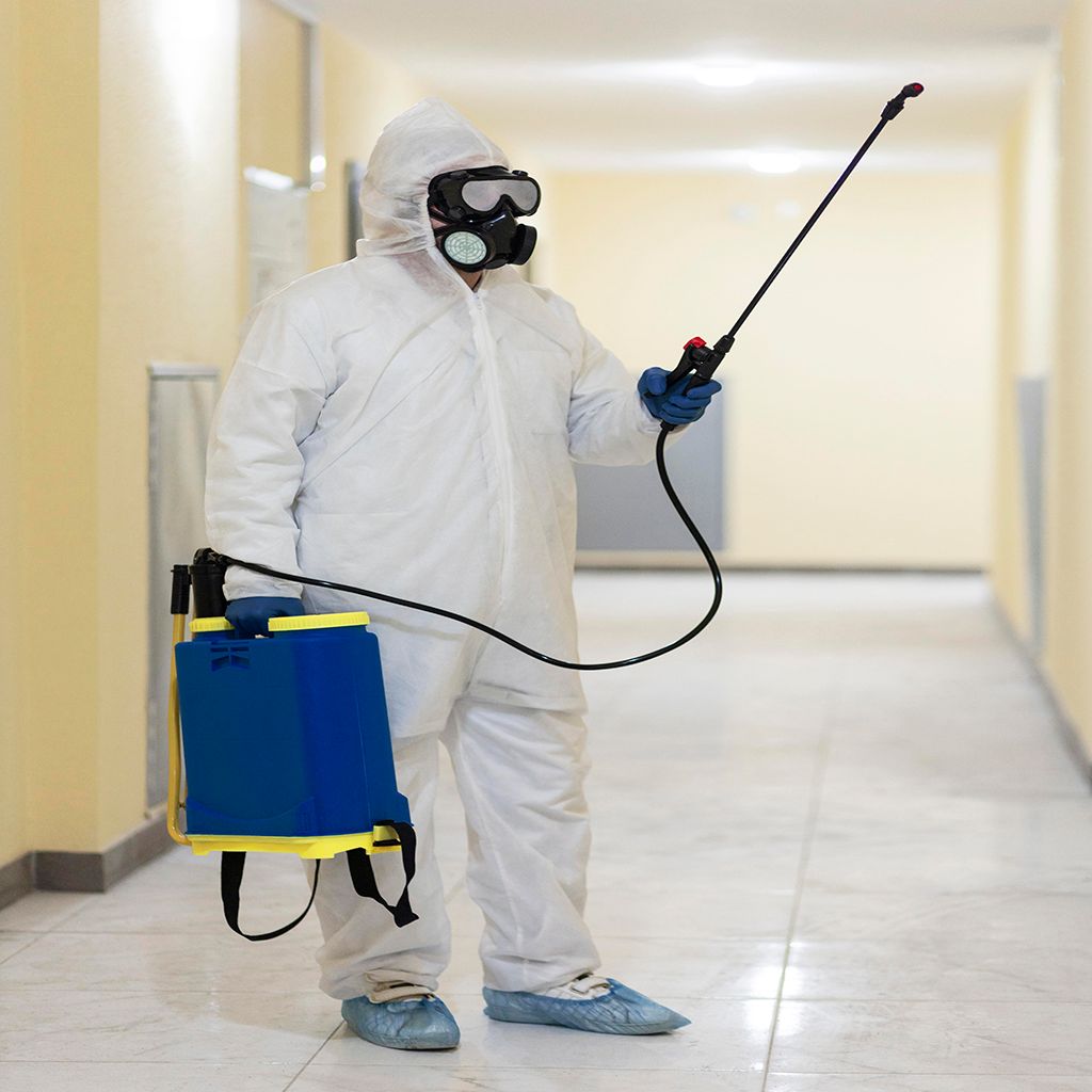A man in a protective suit is spraying something in a hallway.