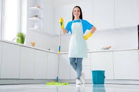 A woman is standing in a kitchen holding a mop and bucket.