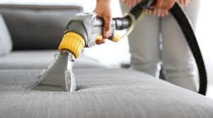A person is cleaning a couch with a vacuum cleaner.