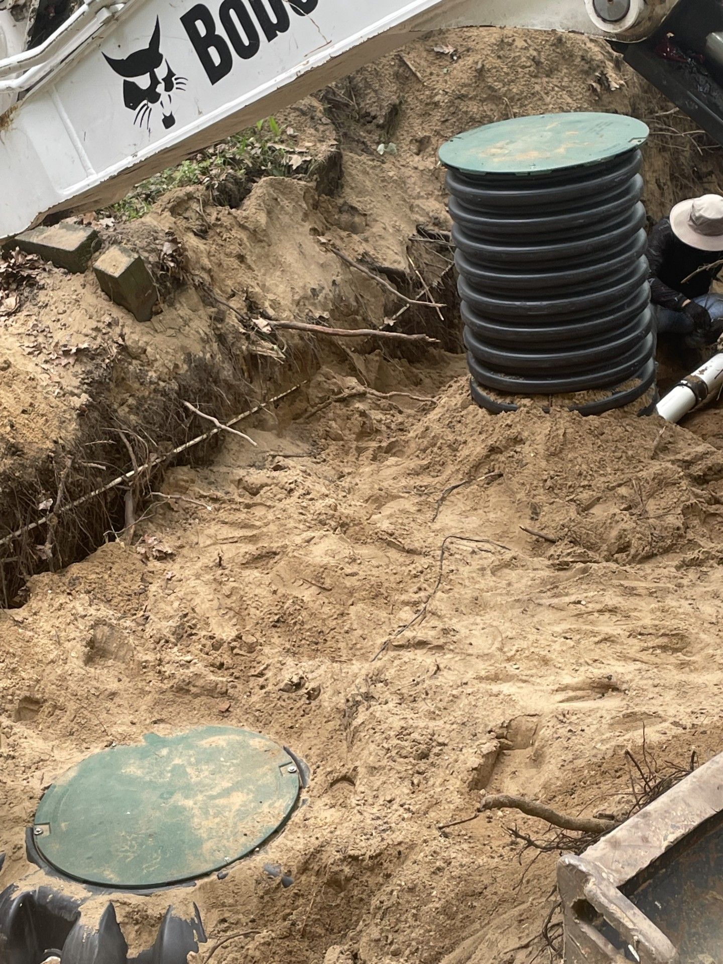 A bobcat is digging a hole in the ground to install a septic tank.