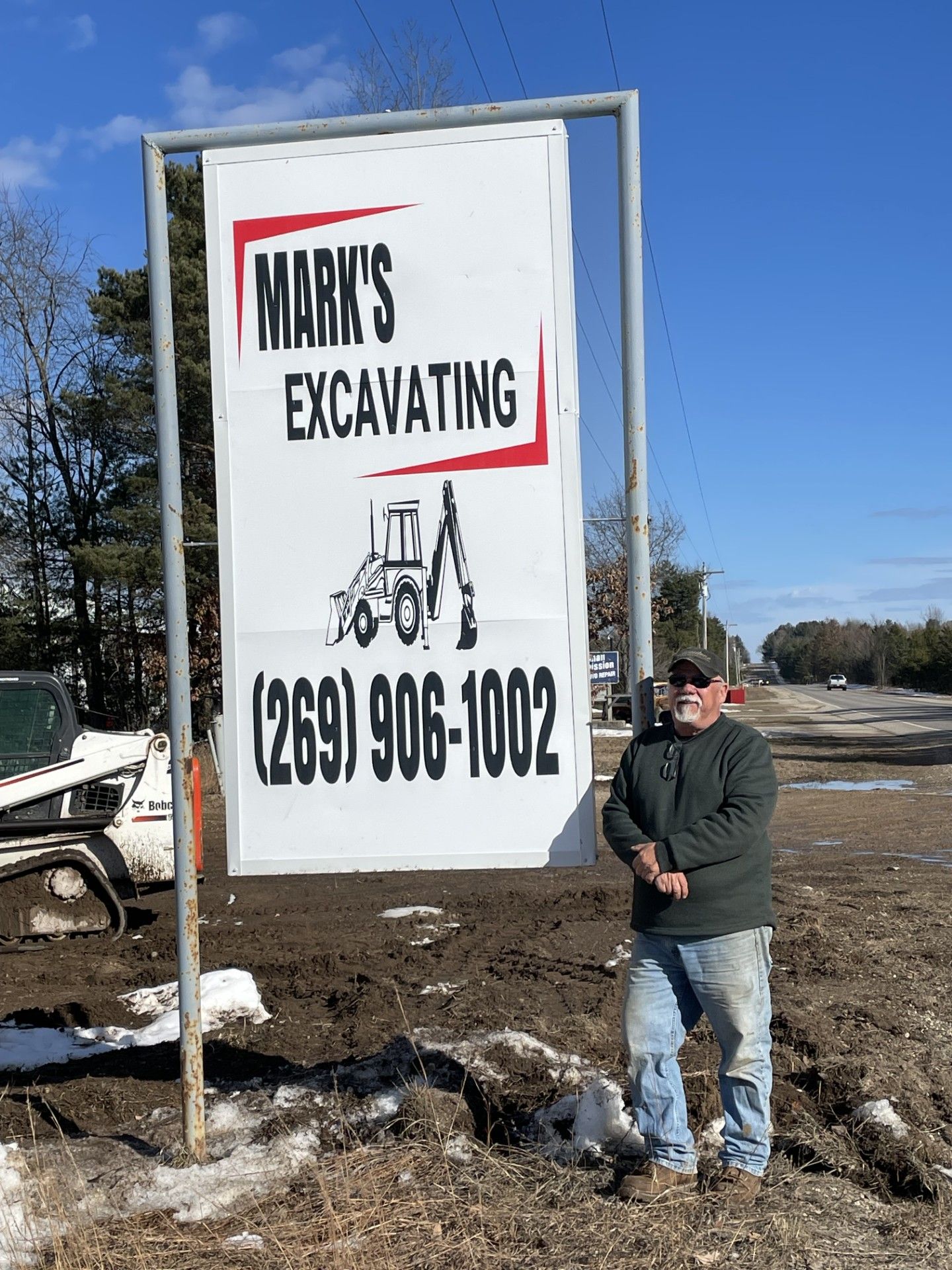 A man is standing in front of a sign for mark 's excavating.