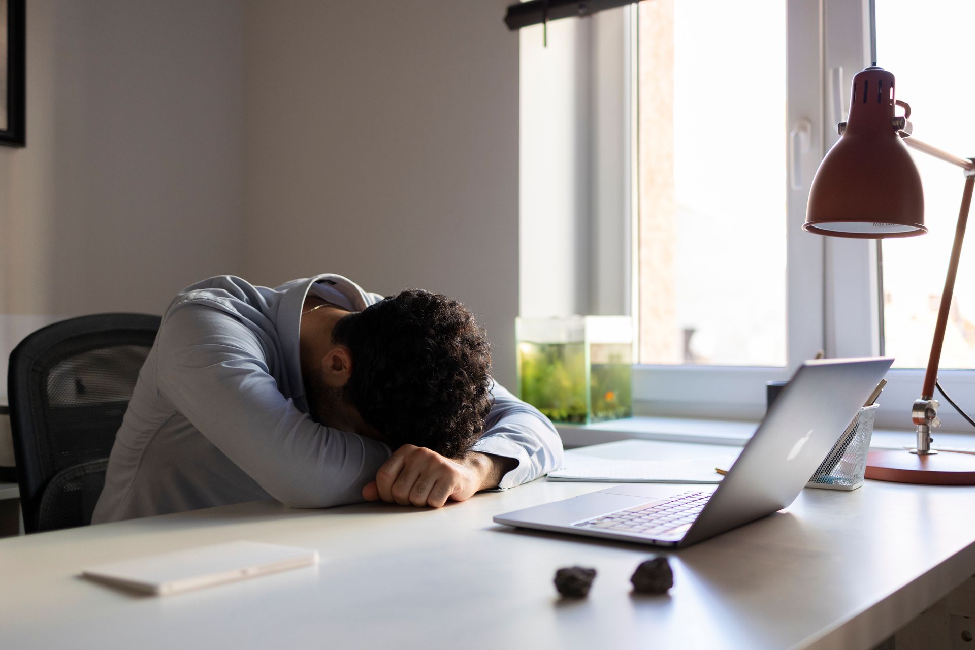 A man is sleeping at a desk in front of a laptop computer.