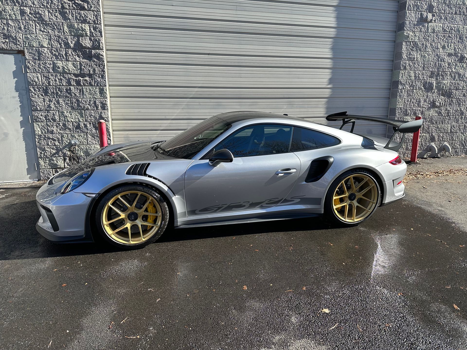 A silver porsche 911 gt3 rs is parked in front of a garage door.