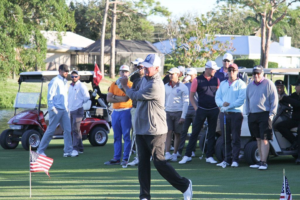 Golfer swings at a golf course, surrounded by spectators and golf carts.