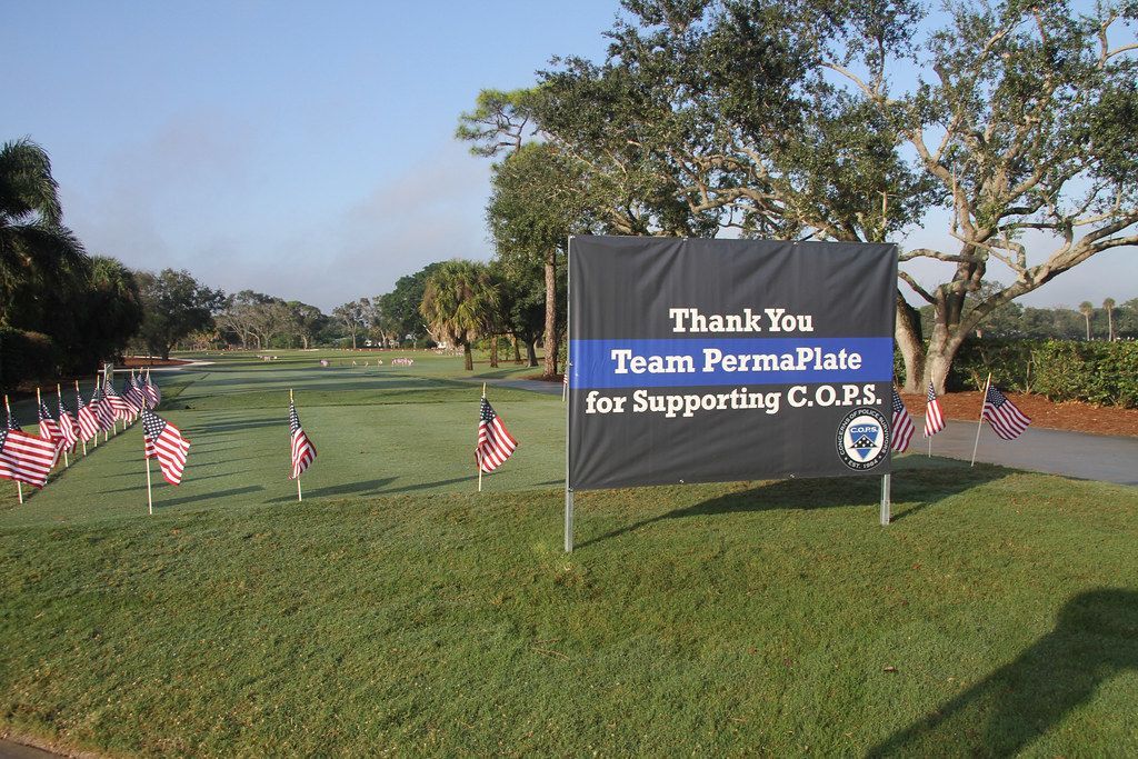 Sign thanking Team PermaPlate for supporting C.O.P.S, with flags on a grassy area.