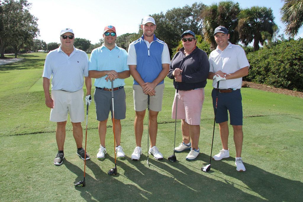 Five men in golf attire stand on a green.