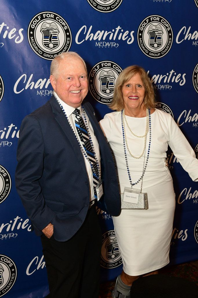 Man in blue blazer and woman in white dress pose together at a charity event.