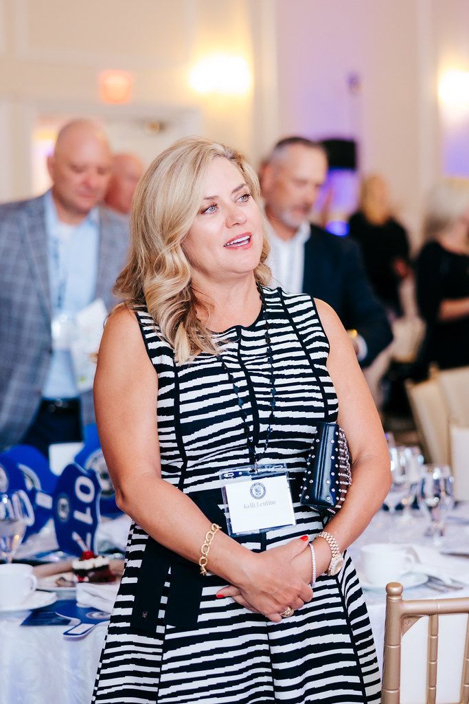 Woman in black and white striped dress at an event, smiling, wearing a name tag.