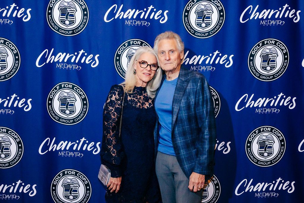 A woman and man pose in front of a blue backdrop at a charity event.