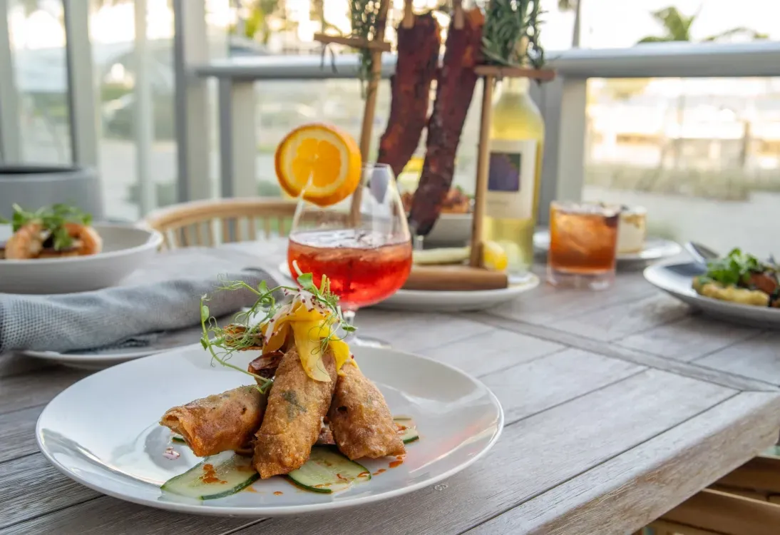 Five men in golf attire pose on a green. Palm trees and a large building are in the background.