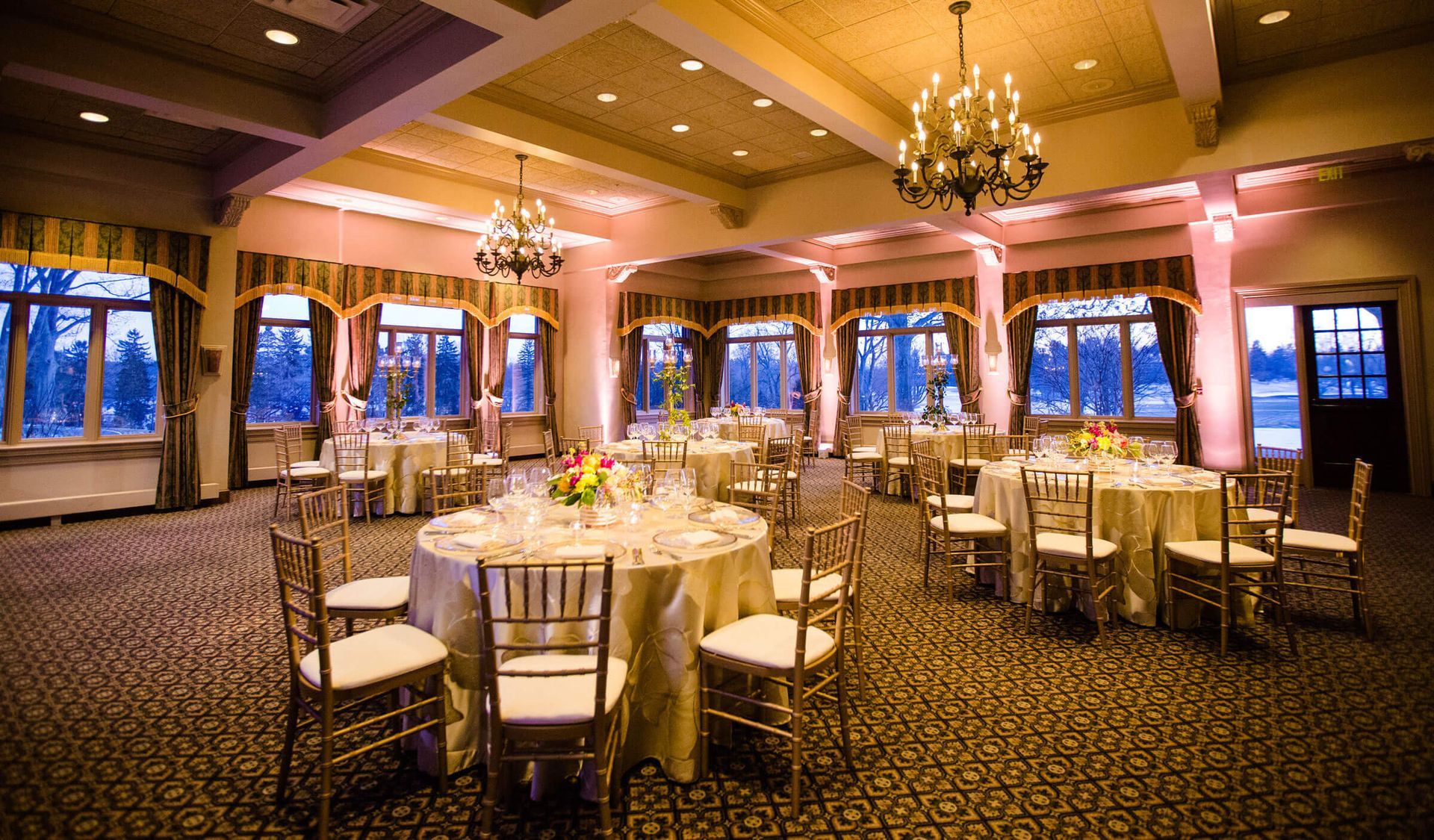 Two people stretch legs on massage tables under a canopy, one assisting the other. Green grass outdoors.