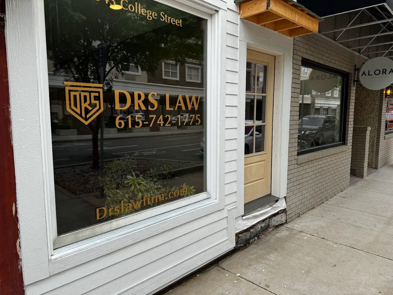 Street-level view of a storefront for DRS Law with its name, logo, and phone number printed on the glass window.