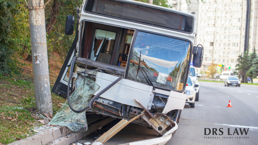 A bus has crashed into a utility pole on the side of a road, with its front windshield shattered and bumper damaged.