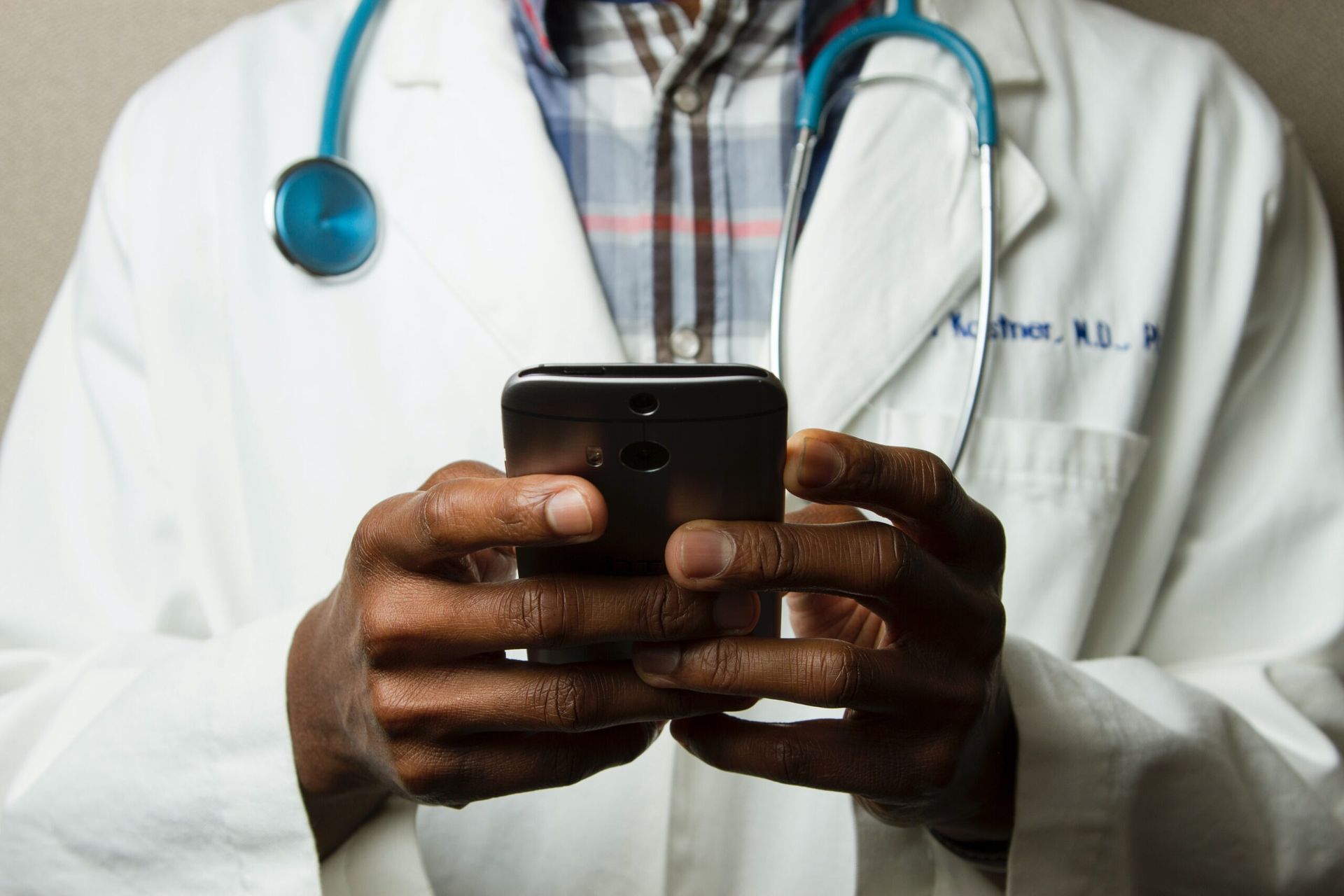A person in a white lab coat and stethoscope holds a smartphone in their hands.