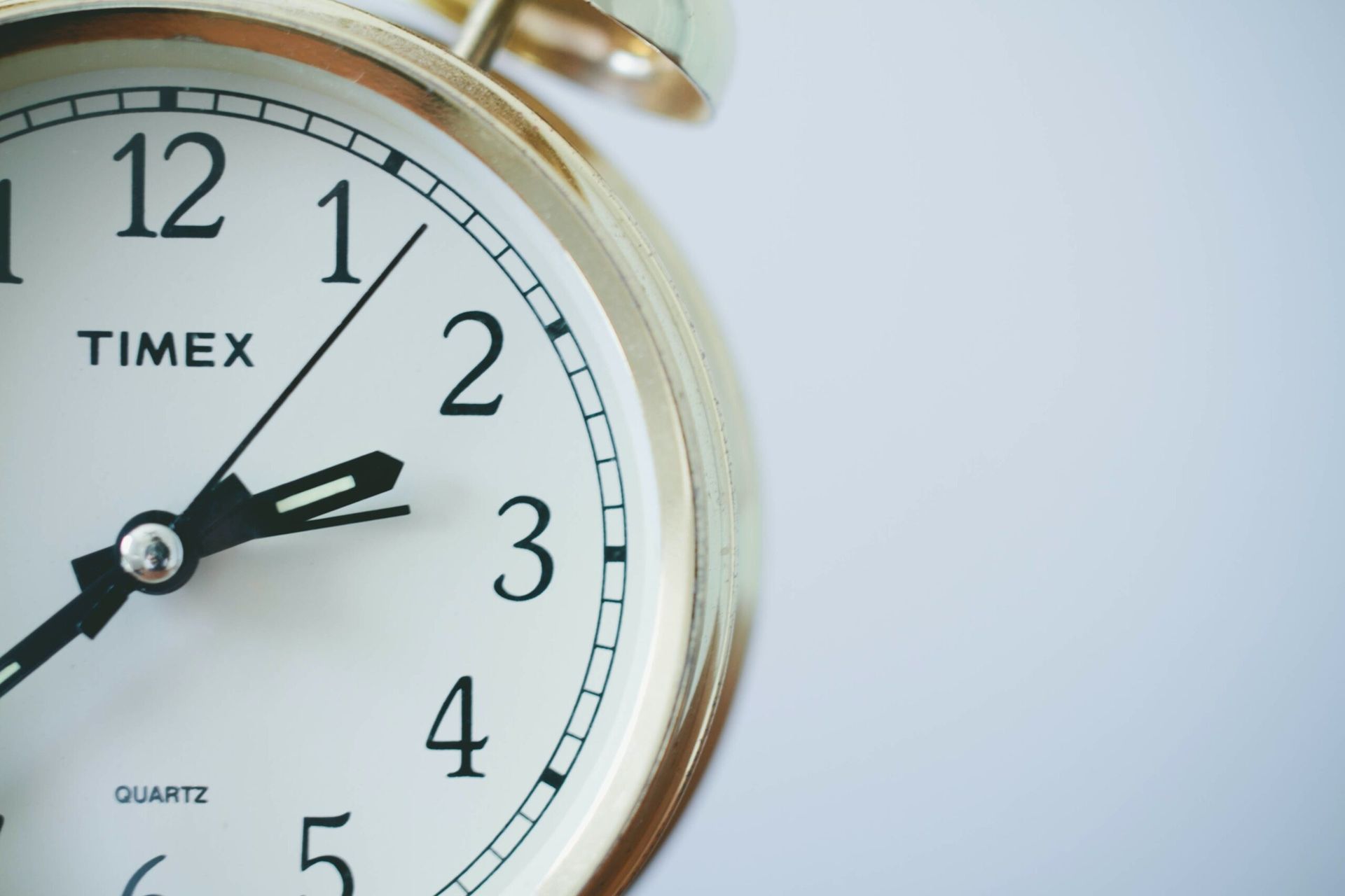A gold-rimmed Timex quartz analog alarm clock showing the time at approximately 1:12.