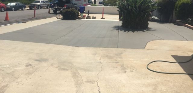 A concrete driveway is being cleaned with a hose.