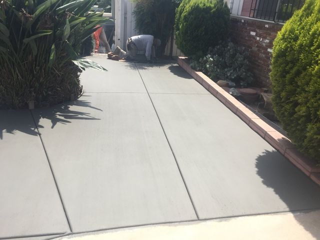 A man is working on a concrete walkway surrounded by trees