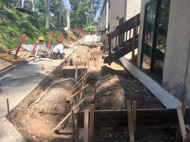 A man is working on a sidewalk in front of a house.