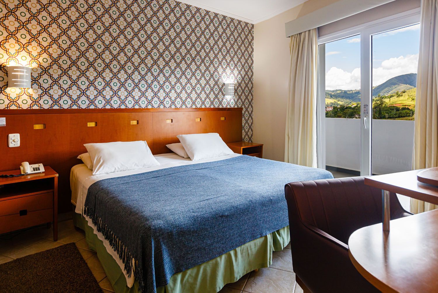 Um quarto de hotel com uma cama, escrivaninha, cadeira e portas de vidro deslizantes.