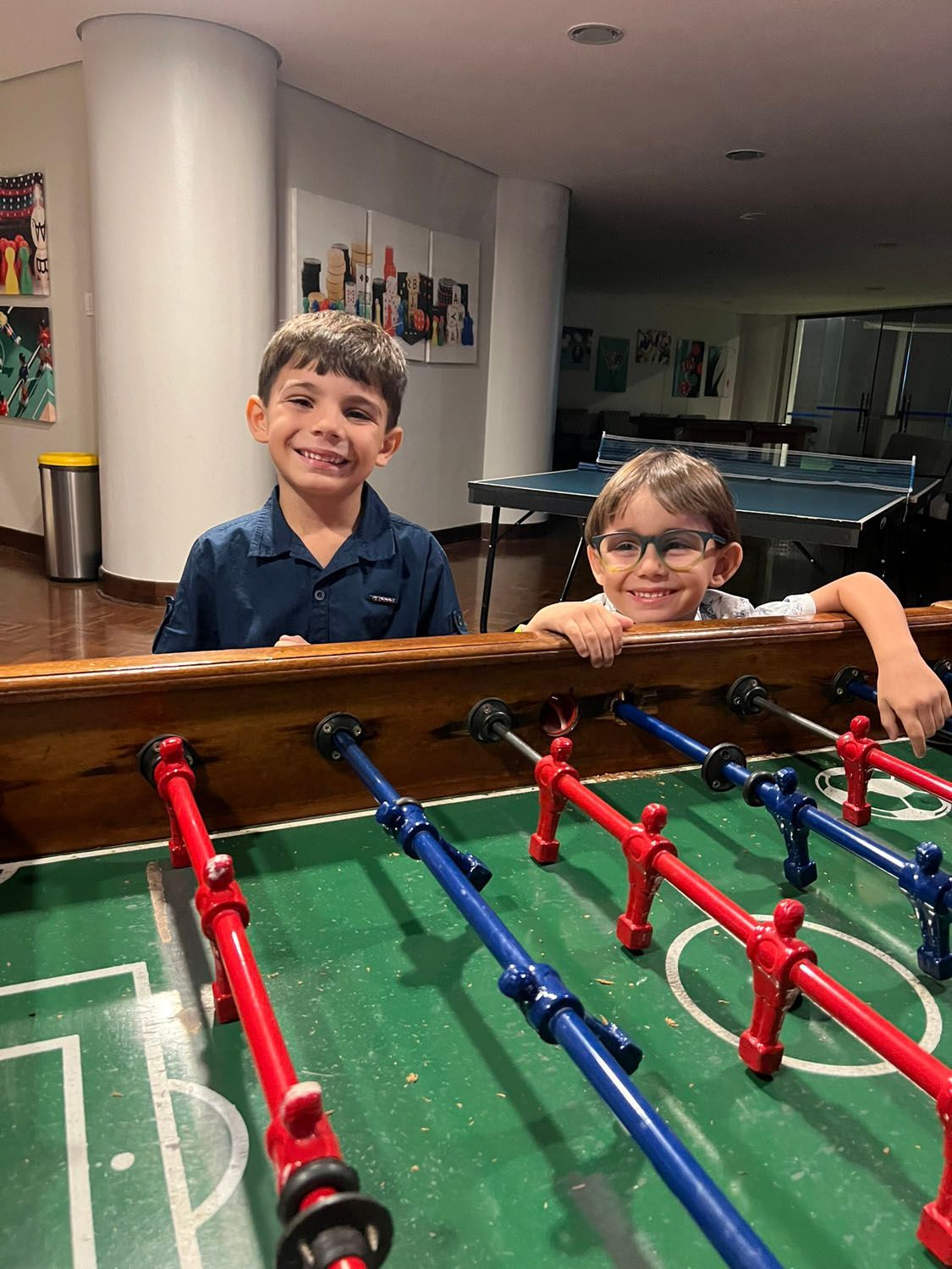 Dois meninos estão sentados em uma mesa de pebolim.