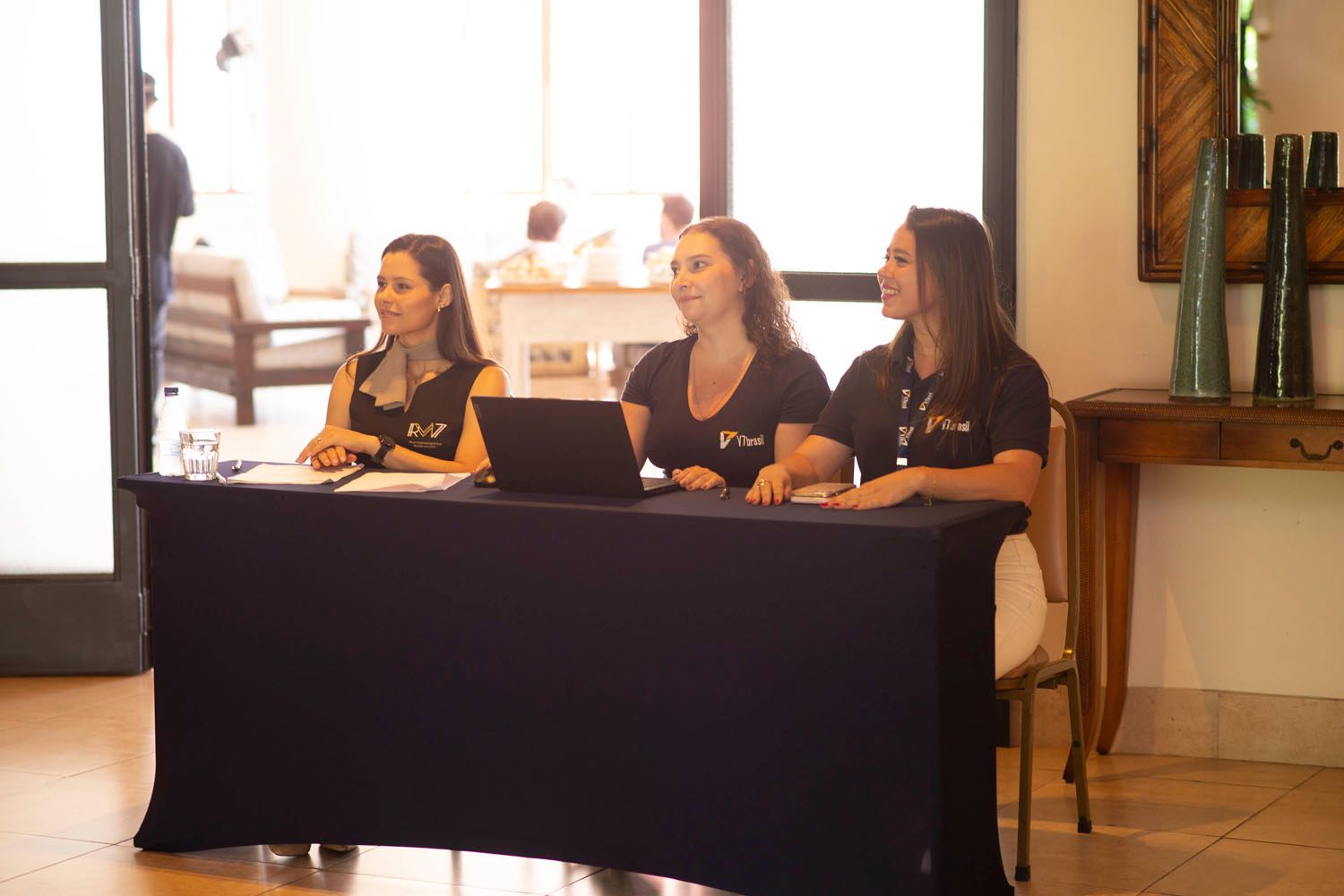 Três mulheres estão sentadas à mesa com laptops.