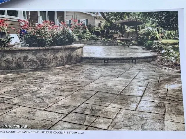 Stone patio with patterned paving, raised planter, flowers, and a curved garden path beside a building