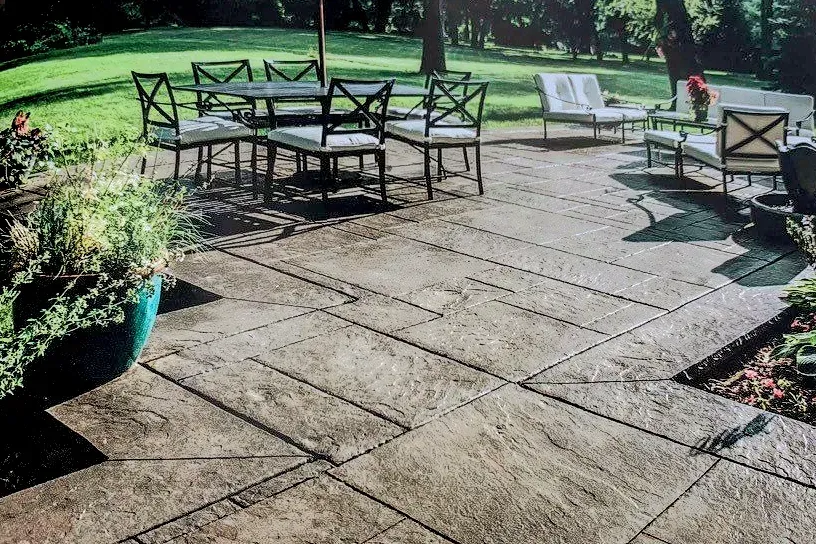 Patio with outdoor table and chairs on a stone terrace, with potted plants and a grassy lawn nearby