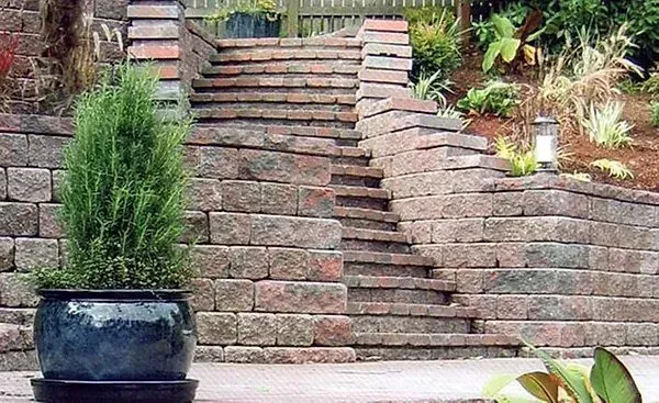 Brick garden steps beside a retaining wall, with a potted evergreen in the foreground