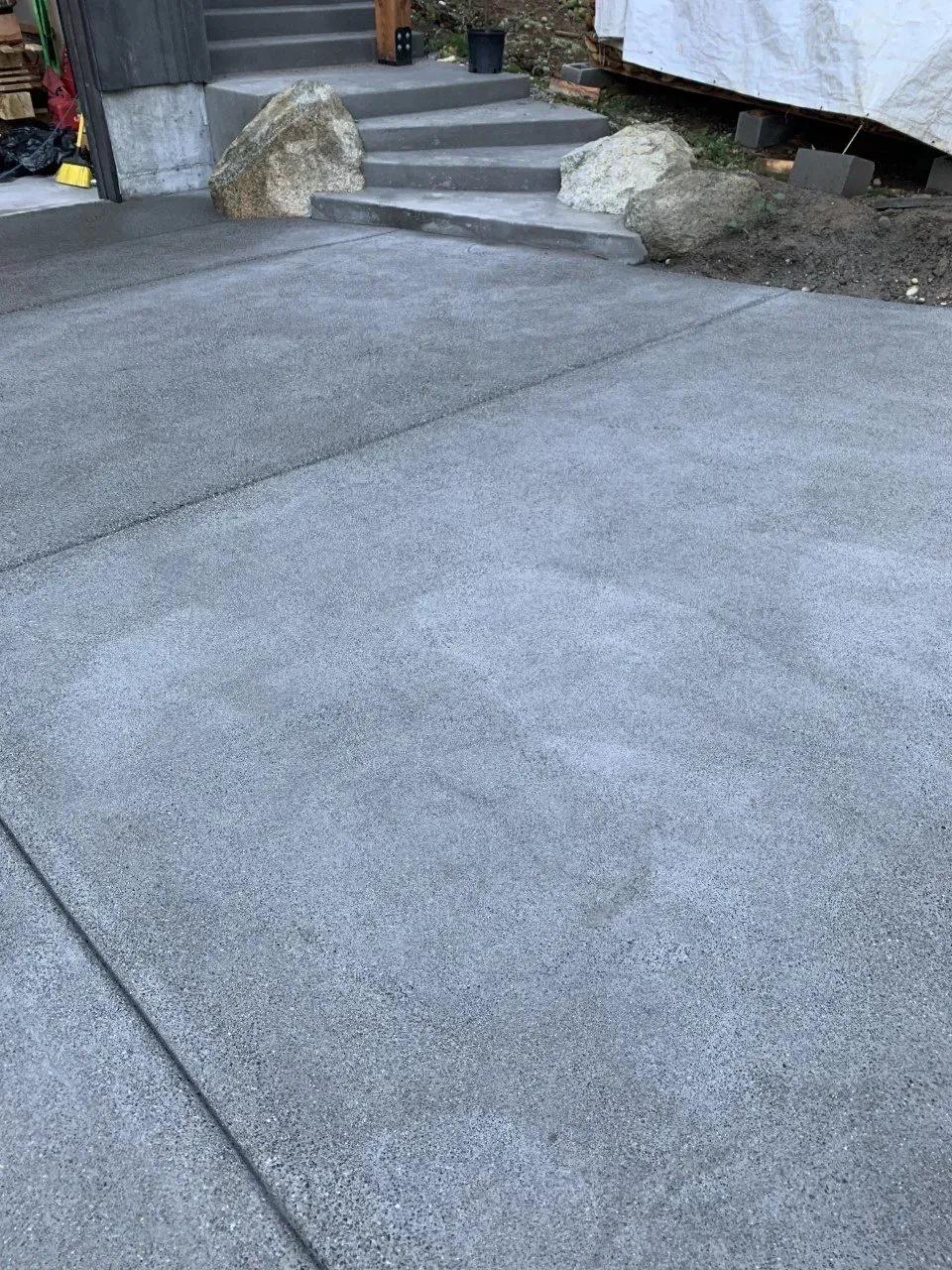 Gray asphalt driveway leading up steps beside rocks and a building edge